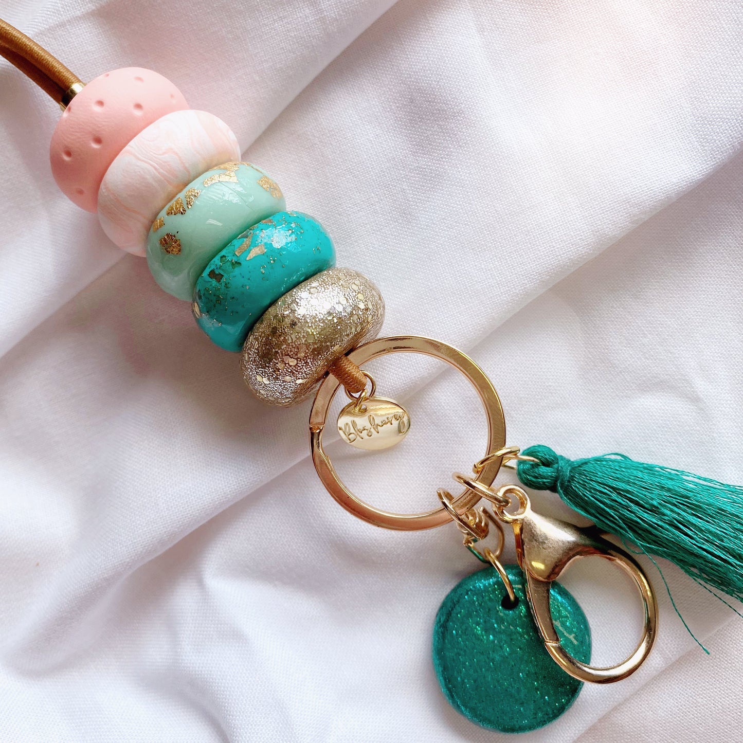 peach and teal lanyards have a gold plated clasp, a teal tassel and teal glitter charm